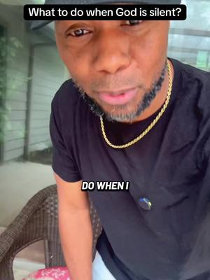 A close-up shot of a Black man looking directly at the camera, set against a blurred background. He's wearing a black t-shirt and a gold chain necklace. Text overlays at the top and bottom of the image.