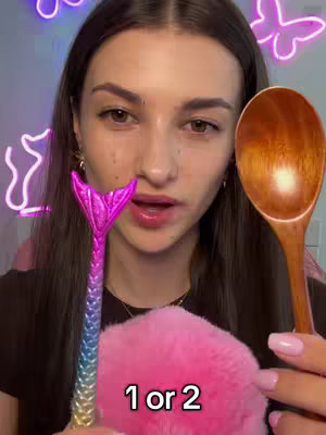 A woman is holding a wooden spoon and a mermaid-tail pen, with a pink fluffy object in her other hand. Text overlayed reads '1 or 2,' and neon butterfly decorations are in the background.