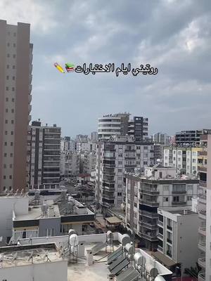 An aerial view of a city with a mix of high-rise buildings and lower structures under a cloudy sky. The foreground includes the tops of several buildings with visible rooftop elements like water tanks and satellite dishes.