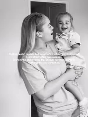 A black and white photo of a woman holding a young child. The woman is looking down at the child with an open mouth, and the child is looking up and laughing. The background is uncluttered, with a door frame and neutral wall visible. Text is imposed over the image in a sans-serif font.