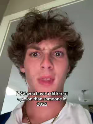 A selfie-style shot featuring a young man with curly brown hair, an intense expression on his face, and a gold chain. The lighting is natural, the background is a plain wall illuminated by a light fixture. Text overlay at the bottom.