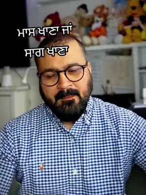 A medium shot of a man with a beard and glasses, wearing a blue and white checkered shirt, looking downwards with his eyes closed. Text overlays in a foreign script at the top of his head.