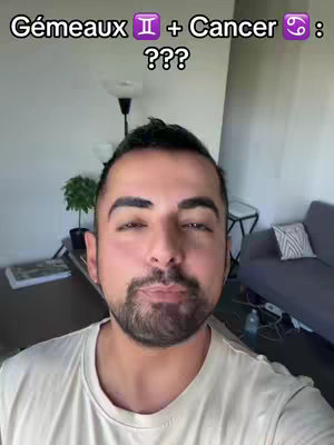 The cover image features a man in a light-colored t-shirt standing in what appears to be a living room. The man is the primary focus, framed from the chest up, with a neutral expression. The background includes a sofa with decorative pillows, a floor lamp, and a glimpse of other furniture. Overlaid text at the top reads "Gémeaux + Cancer : ???".