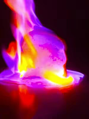 An abstract image featuring a fiery display. At the center, an amorphous shape, possibly bread, is engulfed in vibrant flames. The flames emanate yellow, orange, and pink hues, adding dynamism and intensity. The background is a dark, solid color, providing contrast. The composition evokes a feeling of heat and transformation. The bread shows an abstract pattern on top