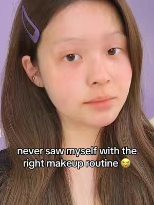A close-up shot featuring a young woman with long brown hair, a purple hair clip, and subtle makeup. She is gazing directly at the camera with a slight expression. Text overlay states 'never saw myself with the right makeup routine'.