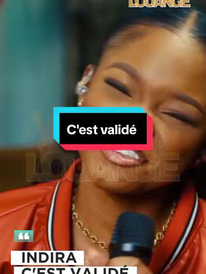 A close-up shot of a woman singing into a microphone. She is wearing a red and black jacket and a gold necklace. Text overlays on the image include "C'est validé" in a colorful banner and the name "INDIRA". The background is subtly blurred, and the overall composition focuses on the subject's face and expression.