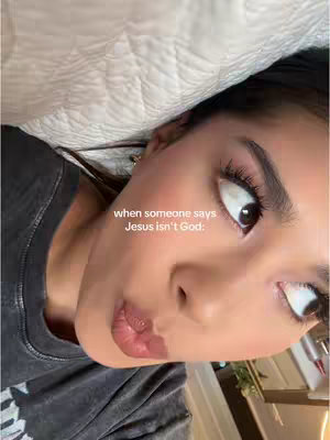 A selfie-style shot featuring a young woman lying down and looking towards the top right corner of the frame. She has dark hair and is wearing a grey shirt. The background includes a soft, white comforter. Overlay text is placed near the upper left third of the image. The lighting is soft and natural.