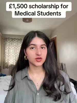 A young woman with long dark hair and gold hoop earrings is speaking directly to the camera. Above her is a text overlay that reads, "£1,500 scholarship for Medical Students" in a bold, sans-serif font. She is wearing a button-down shirt, and a subtle necklace is visible. The background is a room with a bed  and a patterned window treatment.