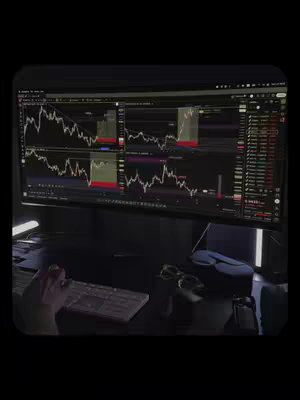 The image shows a dark room where a person is working at a desk, focused on a large computer screen. The screen displays detailed financial charts, with multiple windows showing fluctuating stock data. The person's hand and a keyboard are visible, suggesting they are actively trading or analyzing market trends. The room has a dim, modern aesthetic, with a keyboard and glasses on the desk.