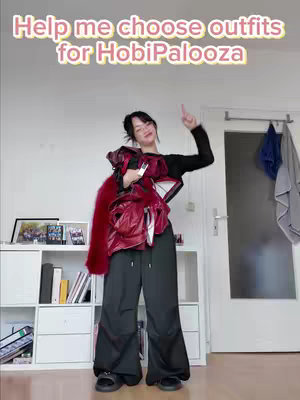 A woman poses with multiple outfits, holding them up with one arm and pointing upwards with the other hand. She is in a room with white walls, a white bookshelf and a door in the background. The text overlay reads: Help me choose outfits for HobiPalooza.