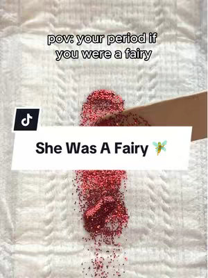 The image shows a sanitary pad with a spread of red glitter, mimicking blood. A hand holds a wooden stick above the glitter. Text overlays read "pov: your period if you were a fairy" and "She Was A Fairy".