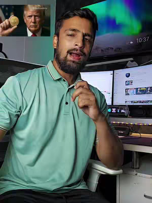 A man with a beard and a light green shirt is sitting in front of two computer monitors. The video has a smaller image in the upper left corner of Donald Trump holding a gold coin.