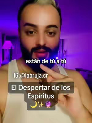 The image is a selfie-style video cover featuring a man with a beard and styled, light-colored hair. He's indoors, with a purple or magenta-toned background. The man is holding something in his hand. Overlayed text includes the creator's Instagram handle (@labruja.cr) and a line of text. There's also an icon of a crescent moon, stars, and a purple crystal ball at the bottom of the block.
