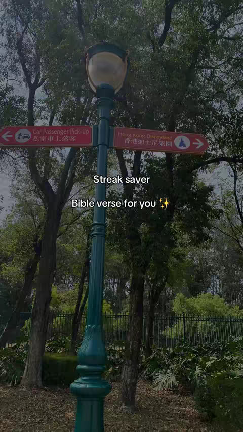 A vertical shot of a green lamppost with directional signs pointing left and right, set against a background of trees and foliage. Overhead text overlays include the words "Streak saver" and "Bible verse for you". The image has a soft, natural lighting.
