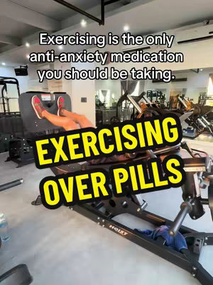 The image appears to be a promotional shot for a health-related video or webinar. It shows a person's legs and feet in red shoes on a leg press machine at a gym, against a backdrop with additional gym equipment and mirrors. Overlaid on the image are two text elements in contrasting colors. The first text reads "Exercising is the only anti-anxiety medication you should be taking." The secondary text which is written in bold, large, yellow letters over the image reads, "EXERCISING OVER PILLS".