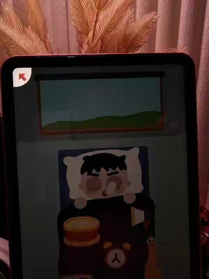 An iPad screen displays a cartoon illustration of a person lying in a bed, a window showing a landscape, and various items on a nightstand. The scene is set with warm lighting.