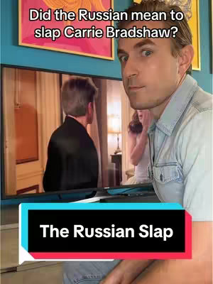 A man is looking towards the camera, with a television screen behind him. The screen is showing a scene of two people in a room. The man in front is wearing a light blue button-up shirt. Above his head, there is a text overlay that says, 'Did the Russian mean to slap Carrie Bradshaw?' Below the screen is a black bar with a text overlay that says, 'The Russian Slap.'