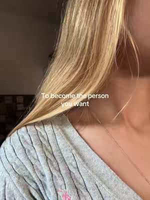 The cover image displays a close-up shot of a person's shoulder and hair. The individual's blonde hair cascades down, partially obscuring their face, and they're wearing a gray sweater with a cable knit design. Text overlayed on the image reads, 'To become the person you want.' The background is softly lit, suggesting an interior setting.