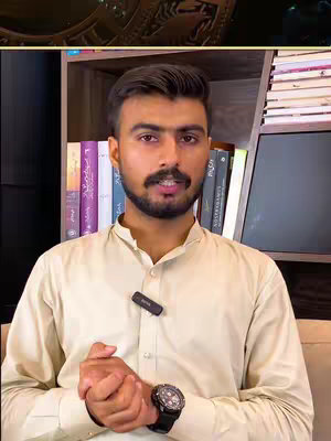 A man with a beard and a cream-colored shirt is speaking to the camera. He is standing in front of a bookshelf with books. The overhead view on the top-left corner shows a logo.