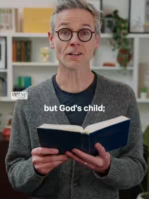 A man with grey hair and glasses is holding a book and talking to the camera, text overlayed on his chest says, "but God's child;". Behind him are white shelves with books, plants, and decorative items.