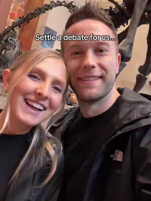 A selfie of a smiling woman and man with a dinosaur skeleton in the background, and text overlay asking to settle a debate.