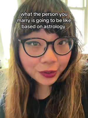 A woman with fair skin and long hair is the central focus, wearing glasses and a black top. Text overlays on the video say, "what the person you marry is going to be like based on astrology."