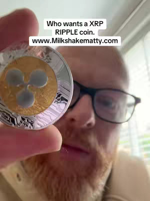 A man with a red beard and glasses holds up a physical XRP Ripple coin, displaying it towards the camera. Text on the image asks, 'Who wants a XRP RIPPLE coin.'