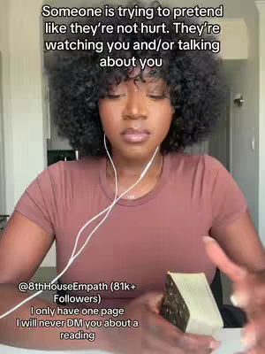 A medium shot of a Black woman with voluminous dark hair and a brown top, wearing white earbuds, holding a deck of cards, with overlaid text. The background appears to be indoors with neutral tones.