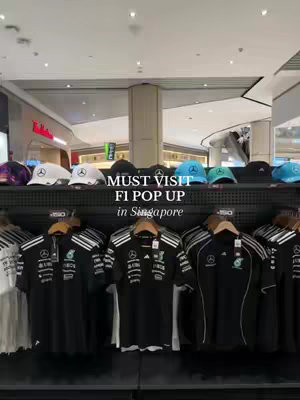 The cover image showcases an F1 merchandise store display. The shelves are neatly arranged with various items, including black polo shirts with racing team logos, and baseball caps on the top shelf. The shop appears well-lit, and the products are arranged in rows.