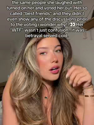 A close-up shot of a young woman with long, wavy blonde and brunette hair. Her expression is one of slight surprise or concern, with parted lips. She has a delicate necklace and is wearing what appears to be makeup. The background is blurred, suggesting a focus on the woman.