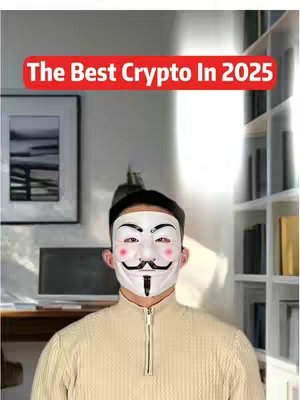 A person wearing a Guy Fawkes mask stands in front of a light brown background, in front of a bookcase. The person is wearing a tan sweater and the text overlay at the top says "The Best Crypto In 2025".
