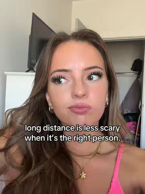 A young woman with long brown hair and a pink top looks at the camera with a slightly pensive expression. Text overlayed on the image reads, 'long distance is less scary when it's the right person.' The background is a blurry interior with a white headboard and a partially opened closet.