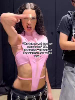 A woman in a pink outfit is winking and pointing her index finger at her temple. Text overlays explain her dancing is due to talent, not her ethnicity.