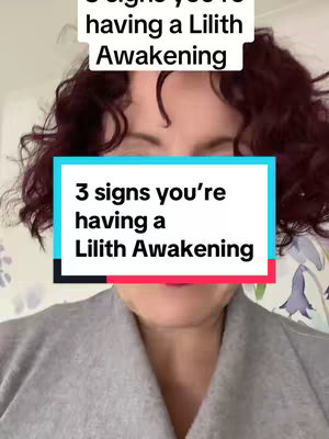 A woman with curly red hair is centered in the frame, with a text overlay that reads '3 signs you're having a Lilith Awakening'. Behind her a floral wallpaper is visible.