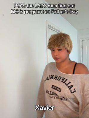 A person with short blonde hair is centered in the frame, wearing a grey sweatshirt. Above, white text overlays reads "POV: the LADS men find out MC is pregnant on Father's Day". Below the person's image is the text"Xavier". The background consists of a white wall and a doorway. The lighting is natural. The overall composition is straightforward, focusing on the person.
