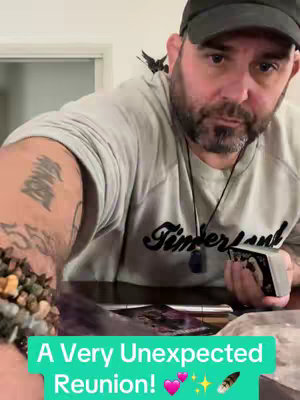 The cover image features a medium shot of a man with a dark beard and cap, holding tarot cards. Text overlayed at the bottom reads "A Very Unexpected Reunion!" in a green box. The man has a black object on his shoulder.