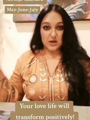 A medium shot of a woman facing the camera, set against a blurred background. She has long, dark hair and is wearing a patterned, light-colored top. Text overlays at the top and bottom provide context.