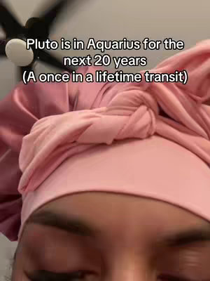 Close-up shot of a person wearing a pink head covering, with text overlayed. The person's eyes and forehead are visible, and parts of a ceiling fan are in the background. The text reads 'Pluto is in Aquarius for the next 20 years (A once in a lifetime transit)'.