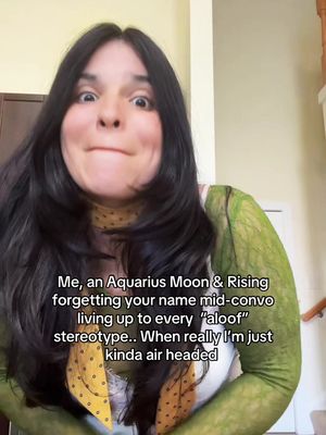 A selfie-style video cover featuring a woman with long, dark hair and a slightly perplexed expression. She is wearing a patterned top. Text overlayed on the image humorously references Aquarius traits.