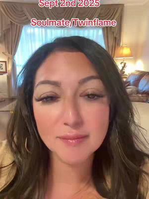 A woman with long dark hair is centered in a selfie-style video. The background shows a well-lit room with curtains and a lamp. Above the woman's head, overlay text in a red font reads "Sept 2nd 2025" followed by "Soulmate/Twinflame".