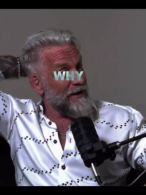 A middle-aged man with a gray beard and hair is the focus. He wears a patterned white shirt and a microphone is positioned in front of him. The word 'WHY' is overlaid across his eyes. The background is plain.