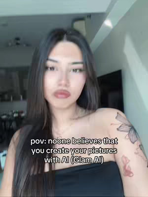 A selfie-style shot featuring a young woman with long, dark hair. She's wearing black, off-the-shoulder clothing. There's a tattoo visible on her upper arm/shoulder. The background is a blurred interior with a light fixture visible. Text is overlaid with the words: pov: noone believes that you create your pictures with AI (Glam AI).