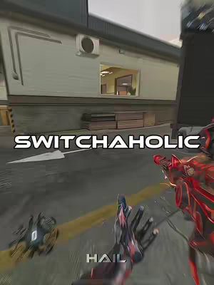 The cover image is a first-person view from a video game within a well-lit outdoor environment, likely a multiplayer first-encounter game. The player's hands holding a futuristic weapon dominate the bottom third of the visual, partially obscuring the view. Along the top portion, a building with an air conditioning unit and window on the left and a partially obscured, shadowed figure on the right of the frame add to the environmental context. The text 'SWITCHAHOLIC' spans horizontally across the center.