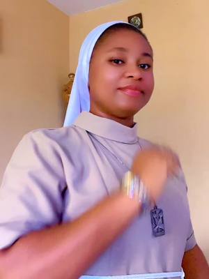 A woman in a white veil and beige clothing is looking toward the camera, smiling. A golden-colored painting is visible on the wall behind her with a clock on top. The woman is wearing a necklace and a bracelet, with a background in beige color.
