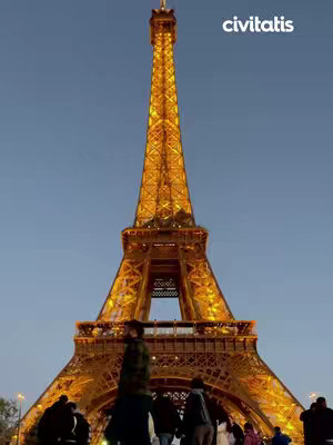 The Eiffel Tower at dusk, bathed in golden light. Silhouettes of people are visible in the foreground.
