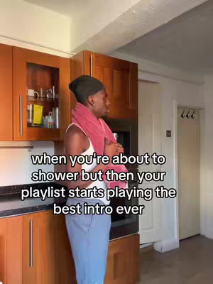 A person stands in a kitchen holding a towel, looking off to the side. Overlay text indicates they are about to shower when a favorite playlist starts playing.