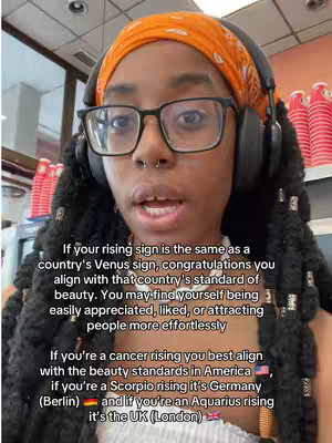 A selfie-style shot featuring a young Black woman with black braids, wearing glasses and headphones. She is positioned in front of a neutral background, with text overlaid on the image containing astrological information.