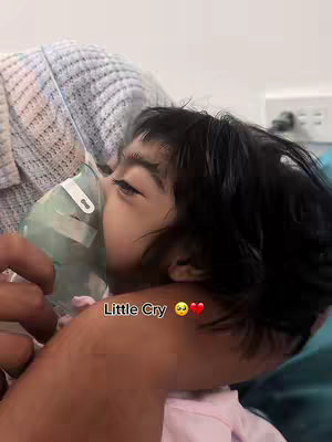 A close-up of a child wearing an oxygen mask, held by an adult. The child's face is visible, with dark hair and closed eyes. The hook text 'Little Cry' is overlaid on the image.