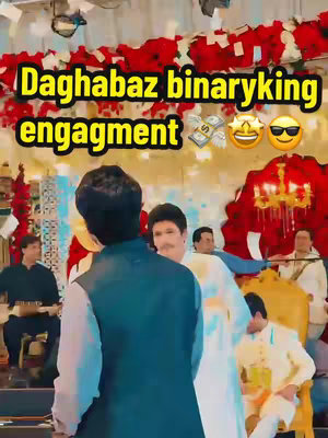 The image is from an engagement ceremony. The foreground features a man in a navy vest over a light blue shirt, viewed from the back, and a person to his right in a blue and white outfit. In the background, thereβs a room decorated with flowers and lights, with additional people. The overlay text highlights the occasion.