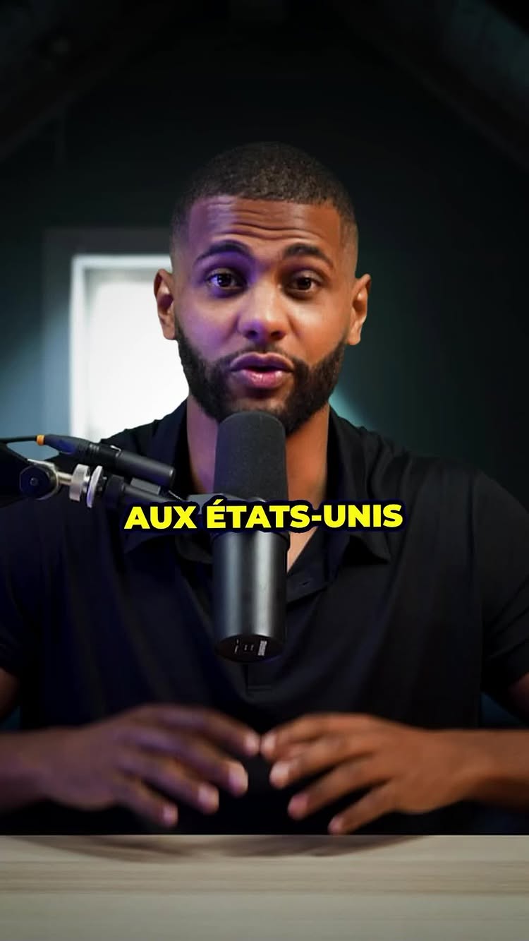 The image features a man in a studio setting with a microphone. He has a beard and is wearing a black shirt. The background is dark. A banner with yellow text is displayed beneath him.